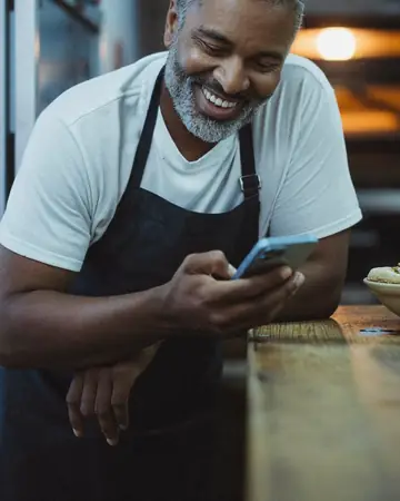 Dono de pizzaria conferindo um pedido no celular no balcão