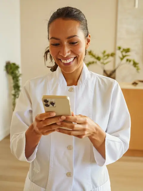 Dentista sorrindo ao ler uma mensagem no celular na recepção clara da clínica