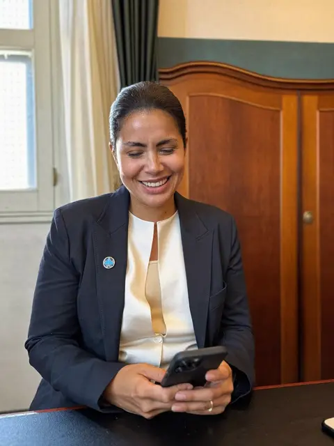 Advogada sorrindo ao ler uma mensagem no celular à mesa do escritório