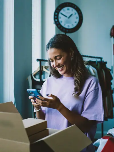 Dona de loja lendo a mensagem de uma cliente ao lado de pedidos embalados